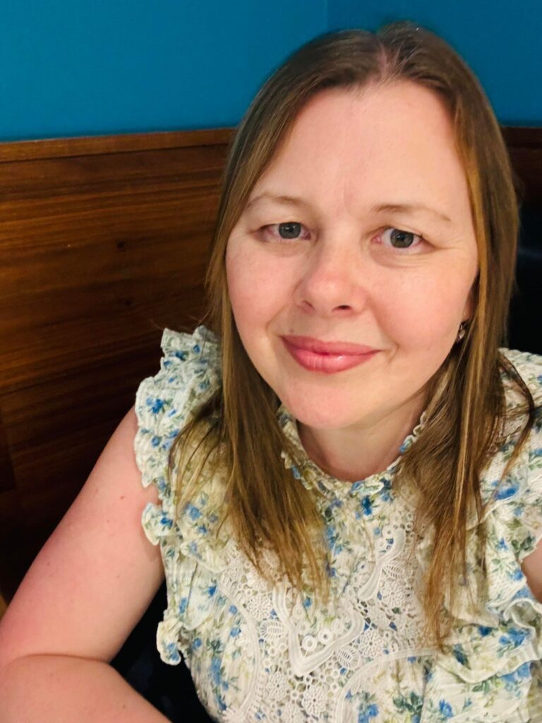 Louisa in front of a blue background wearing a flowery top